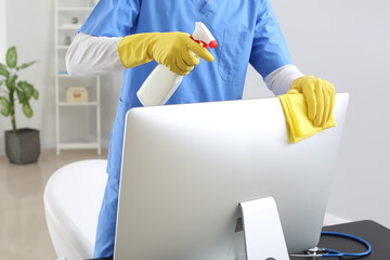 Male janitor cleaning computer in office