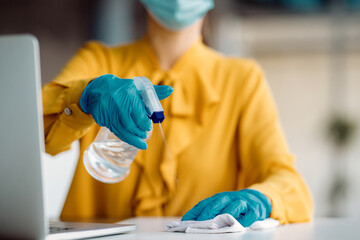 Close-up of businesswoman cleaning her office desk with disinfectant.