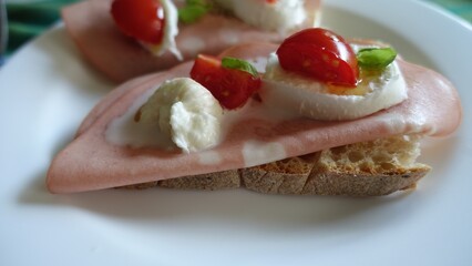 An open sandwich with homemade bread, mortadella, mozzarella, cherry tomatoes, basil