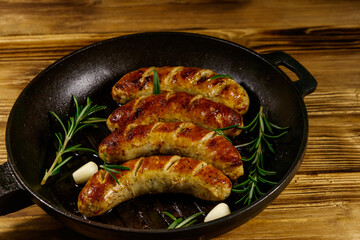 Fried sausages with rosemary, garlic and spices in cast iron grill frying pan on wooden table