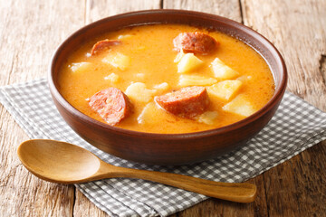 Spicy thick potato soup with sausages and sour cream close-up in a plate on the table. horizontal