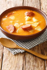 Traditional Hungarian thick potato soup with sausages close-up in a plate on the table. vertical