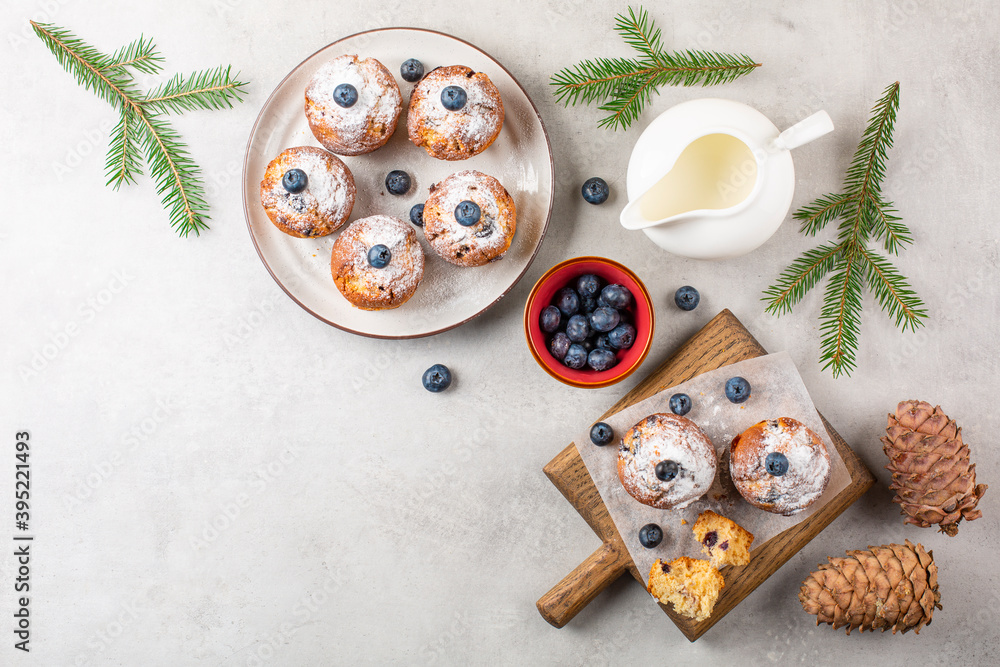 Poster Festive christmas breakfast with blueberry muffins decorated with fresh blueberries and powdered sugar, milk on light grey table , decorated with fir tree branches.  Copy space. Top view.