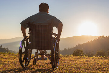 Disabled handicapped man is sitting on wheelchair at sunset.