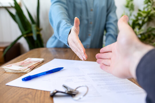 Realtor and buyer handshake. Close up of hands. On the table are money, keys and documents. Rental and purchase of real estate