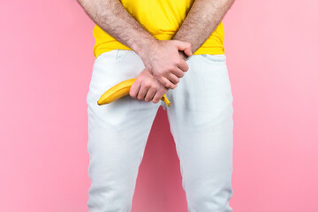 Potency and men's health. A man in white jeans, legs apart, holds a banana near the genitals. Pink...