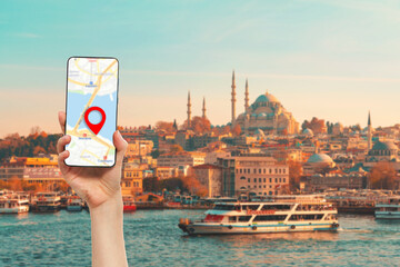 A hand holds a smartphone with an online maps app. In the background, a river with a tourist ship....