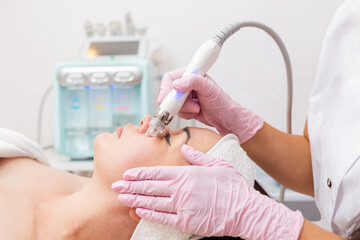 Beauty salon. The cosmetologist performs a water peeling procedure on the client's cheeks. Side...
