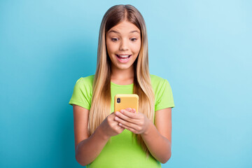 Photo of young amazed happy excited good mood happy girl smiling using cellphone isolated on blue color background
