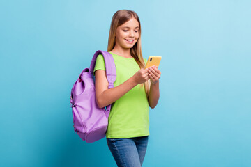 Photo of young smiling cheerful good mood positive girl browsing in internet wear violet rucksack isolated on blue color background