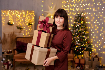 Fototapeta na wymiar young beautiful woman holding heap of gift boxes over christmas background with Christmas tree and led lights