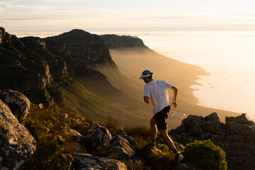 A person running along a mountain top at sunset  - 395230473