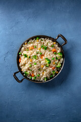 Vegan rice with vegetables, broccoli, carrot and grean peas, shot from above on a blue background with a place for text