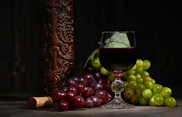 Red wine in glass with vintage bottle and with bunch of red and white grapes on wooden background.
