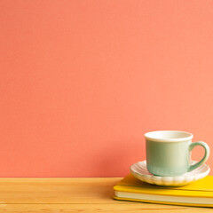 Coffee cup with notebook on wooden table. Pink background