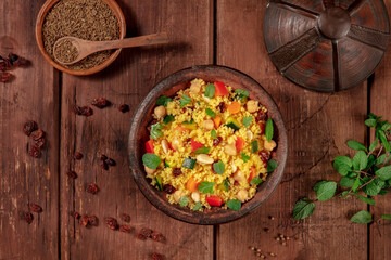 Moroccan couscous, overhead flatlay shot in a tagine with ingredients, on a dark wooden background