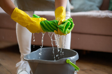 A woman in rubber gloves wrung out a green rag. Professional cleaning service. Cleaning floors with...