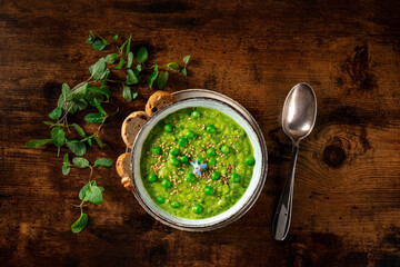 Vegan green soup, shot from the top with toasts and mint on a dark rustic wooden background