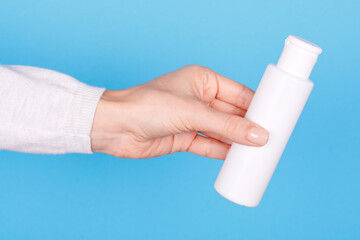 Hand with white lotion bottle on blue background.