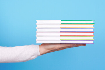 Hand with stack of books on blue background.
