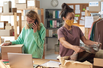 Young two women in protective masks packing clothes into the boxes working in delivery service