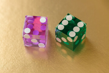 Two multi-colored glass dice, pink and green, against a gold background in sunlight. The result is two and six. Selective focus macro photography.