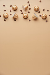 Caffeine, hot drinks and objects concept - close up of golden capsules or pods for coffee mashine with some roasted grains on beige background. Top view with space for text. Flat lay..