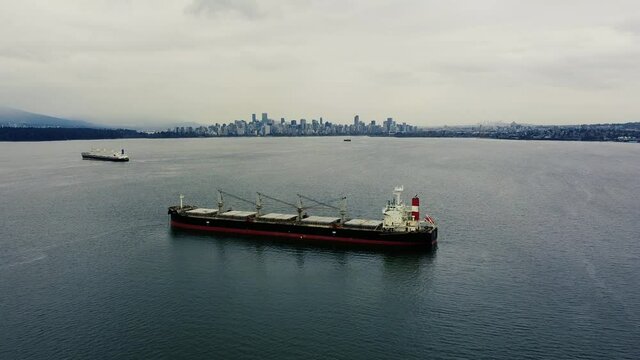Fly over cargo ship and Vancouver downtown on background on a cloudy day