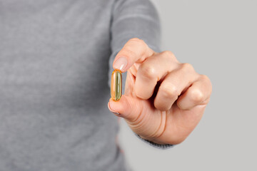 Hand with golden medical pill on grey background.