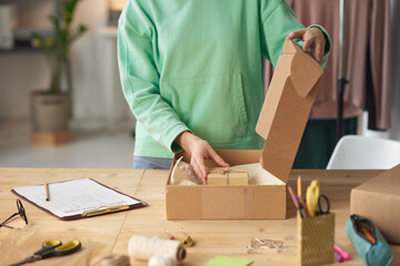 Close-up of young woman putting little present for customer into the parcel
