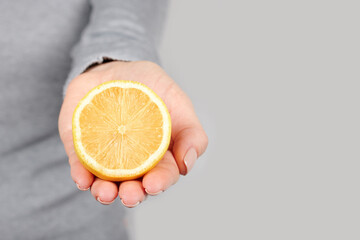 Hand with half lemon on grey background.