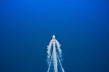 Top view of a white boat sailing in the blue sea. Aerial view of a boat in motion on blue water. Drone view of a boat sailing at high speed.