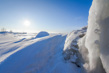 A frozen lake with ice boulders, a bright sun disk with sharp rays and a pier on the horizon