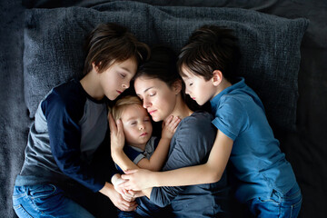 Young mother, hugging her three children in bed, positive emotion, love, happiness