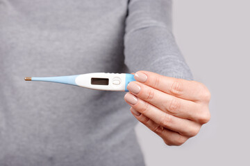 Hand with electronic thermometer on grey background.