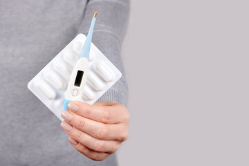 Hand with electronic thermometer and pills blister on grey background.