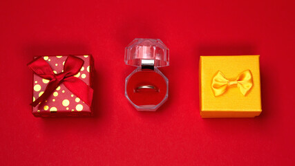 Colorful gift boxes bow presents, golden bright wedding ring marriage proposal on red background. Concept for lover in Valentine's Day, Birthday, New Year or Christmas. Proposing to his girlfriend.