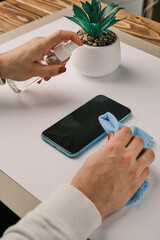 Woman Cleaning And Disinfecting Cell Phone Against Virus on a white desk with home plant