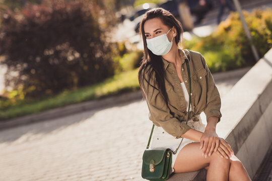 Photo portrait of dreamy woman looking in distance wearing white face mask sitting outdoors
