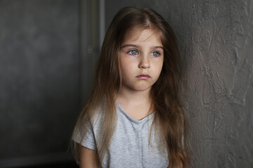 Portrait of cute sad blonde little girl standing by the wall