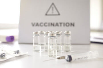 Syringe and glass vials with modern antiviral vaccine placed on white hospital table