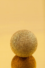 Sparkling golden christmas ball on golden mirror surface, close-up, selective focus. New year composition.