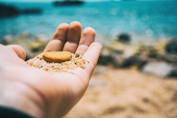 Close-up of a hand holding up a brown pebble and some sand