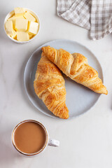 Fresh french croissants on plate, cup of coffee and milkman in the morning light. Continental morning breakfast on marble background.