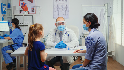 Obraz premium Radiologist with protection mask asking for child x-ray and checking it. Physician specialist in medicine providing health care services consultation treatment in hospital cabinet during covid-19