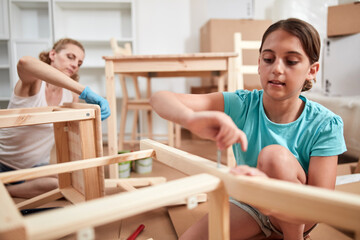 Mother and daughter painting and assembling furniture in new apartment, moving in and being...
