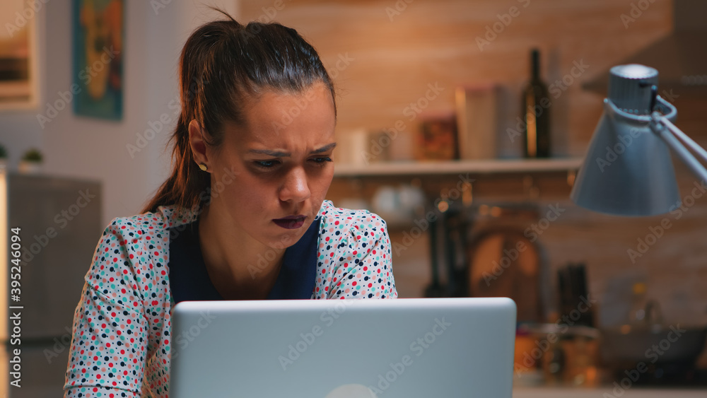 Poster tired freelancer squinting while reading emails working from kitchen home late at night in front of 