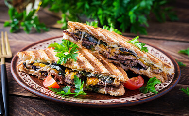 Grilled club sandwich panini with beaf, tomato, cheese and leaf mustard. Delicious breakfast or snack.
