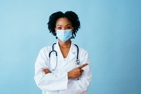 Portrait Of A Doctor In Lab Coat With Face Mask And Arms Crossed Pointing To Side At Copy Space