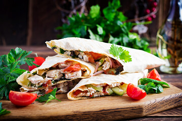 Grilled tortilla wraps with chicken and fresh vegetables on wooden board. Chicken burrito. Mexican food. Healthy food concept. Mexican cuisine